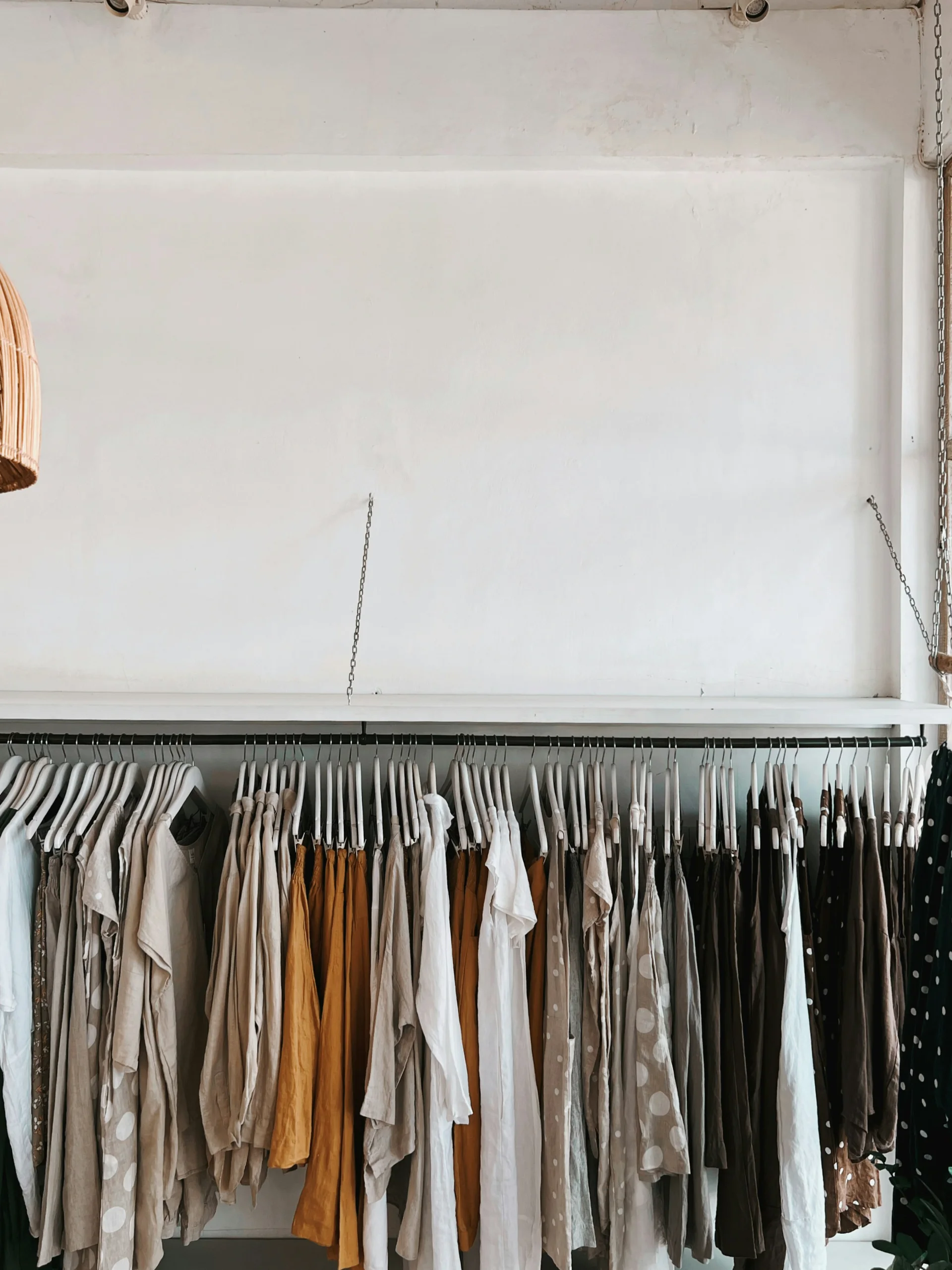 A row of clothes in cream, beige and earth tones hanging on the same rail.